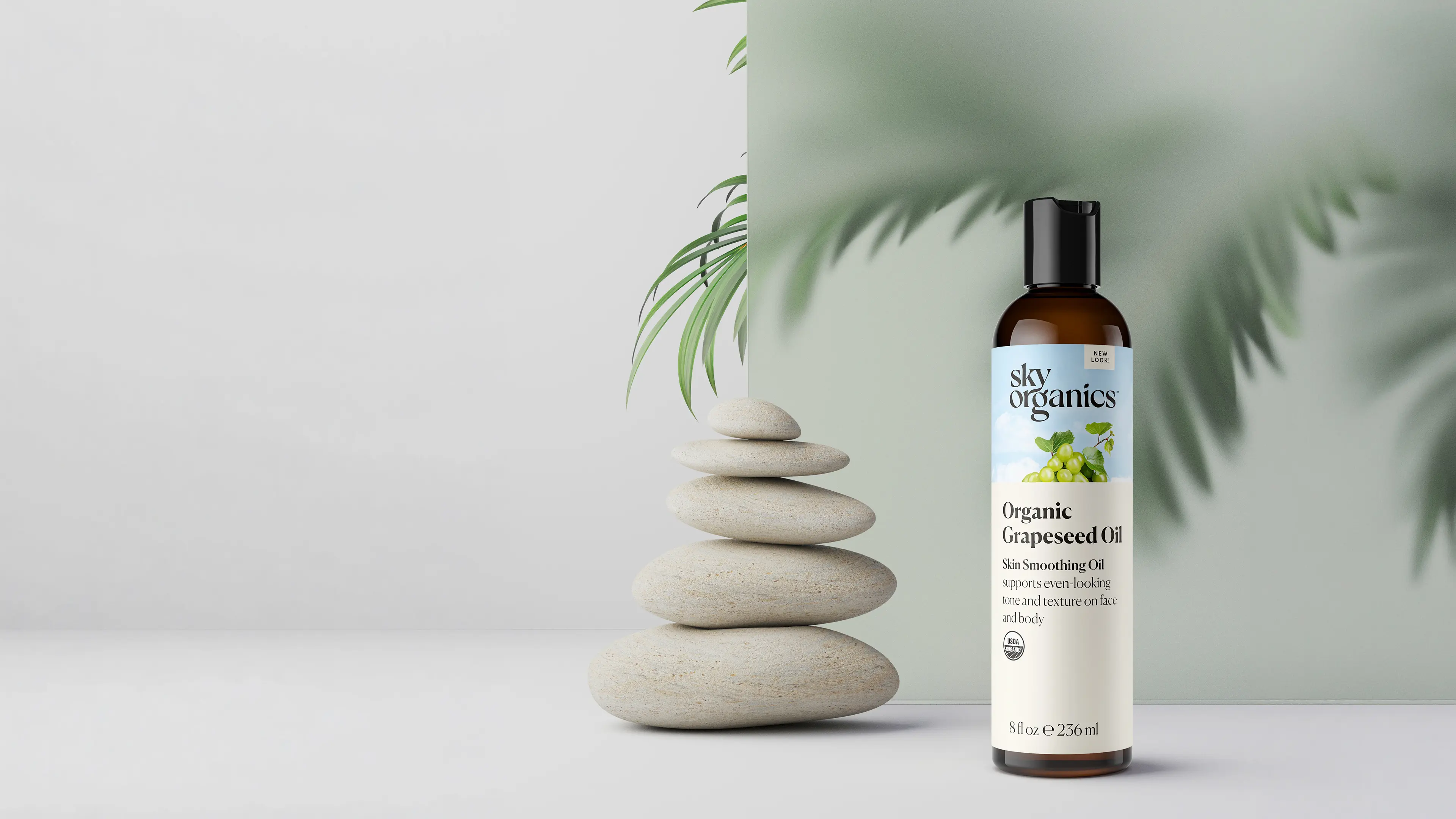 Organic grapeseed oil bottle rendered in 3D beside stacked stones and palm leaves in a calming setting