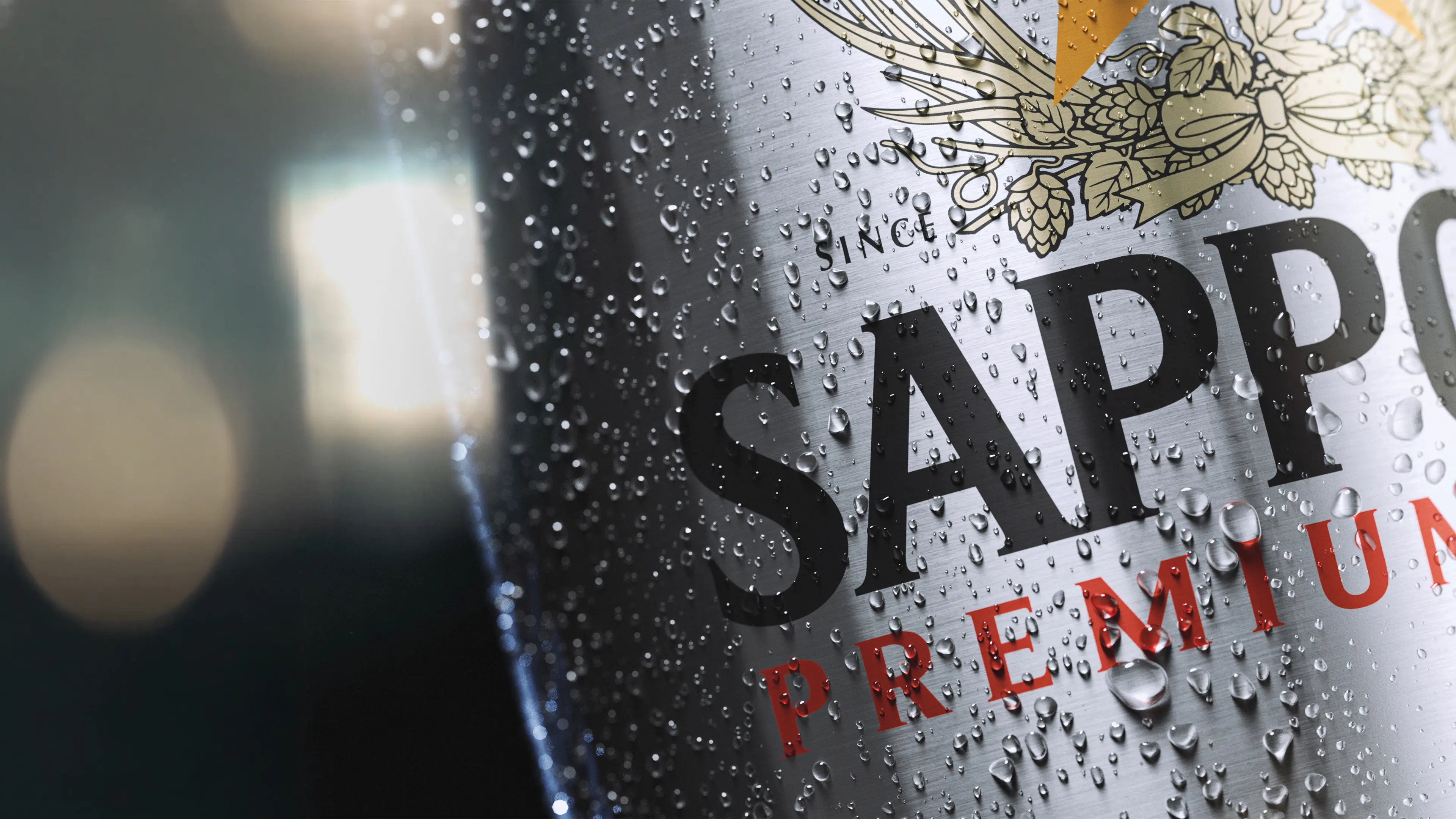 Macro shot of a chilled Sapporo Premium beer can, condensation beads on brushed metal with gold hop artwork